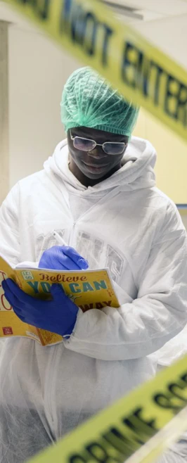 Forensic science student reads instructions behind crime scene tape during a practical lab exercise. Forensic science student reads instructions behind crime scene tape during a practical lab exercise.